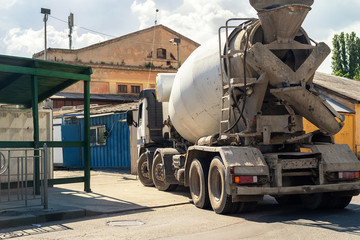 Rear view of heavy concrete cement mixer truck entering construction site with old building on background. Renovation or rebuilding. Urban development industrial scene.