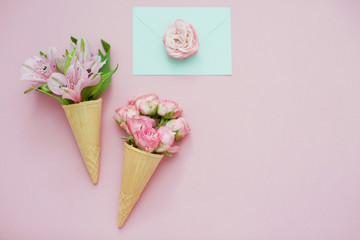 Ice cream cones with pink flowers and mint envelope on pink pastel background