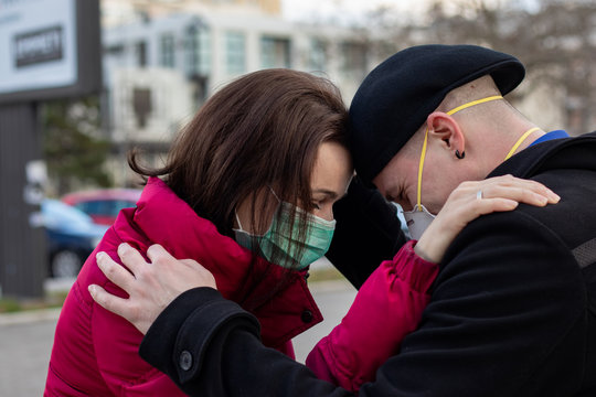 Young couple saying goodbye to each other wearing masks to protect them from viruses, smog or other atmospheric pollutants in the big city. Conceptual photo about health, ecology and air pollution.