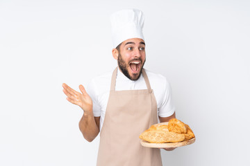 Male baker holding a table with several breads isolated on white background with surprise facial expression