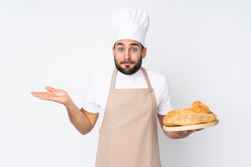 Male baker holding a table with several breads isolated on white background having doubts with confuse face expression