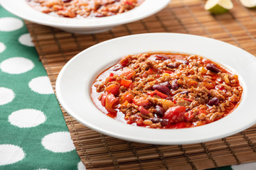 Chili con carne in a white bowl on a served table close-up. Chili con carne - a traditional Mexican soup with beans, tomatoes, minced meat and hot peppers. Mexican cuisine.