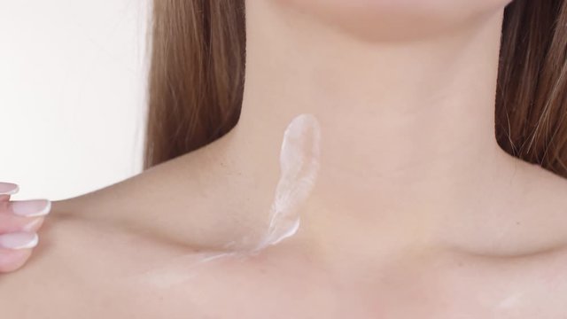 Extreme close up shot of unrecognizable woman with bare chest gently putting moisturizing lotion on her neck and collarbone