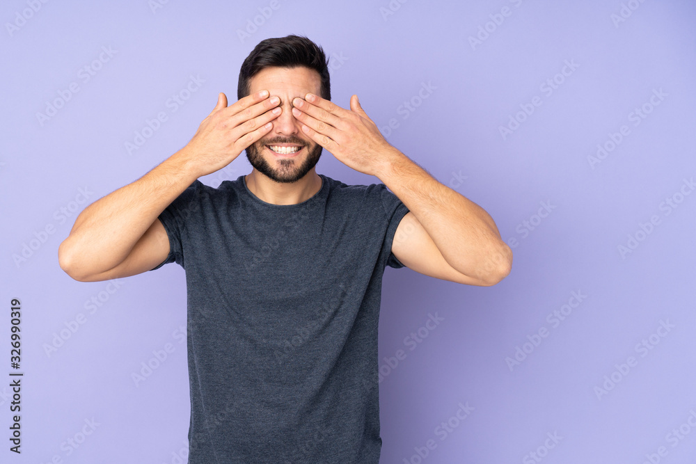 Wall mural caucasian handsome man covering eyes by hands and smiling over isolated purple background