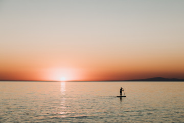 Woman paddling on a board on the sea in sunset