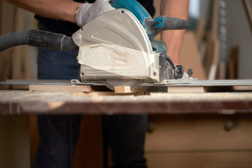 Hands of carpenter male sawing wooden boards with jigsaw