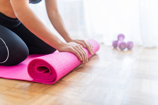 Close-up of attractive young woman folding pink yoga or fitness mat after working out at home in living room. Healthy life, keep fit concepts. Horizontal shot