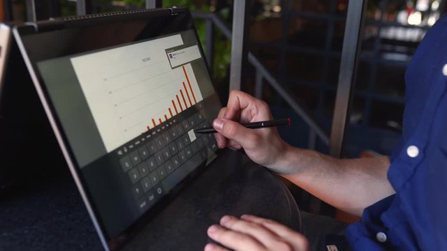 Businessman makes a presentation using stylus and convertible laptop with touchscreen in tent mode. Freelancer type on screen keyboard and use graphic text recognition working with 2 in 1 notebook.