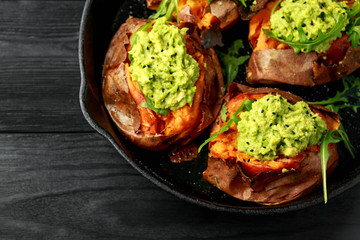 Baked Sweet potato boats stuffed with avocado guacamole and wild rocket sprinkled with nigella seeds in cast iron pan