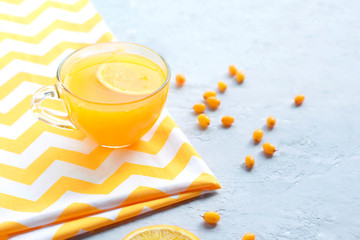 The idea of ​​vitamin tea with sea buckthorn and orange in a transparent cup on a gray background.