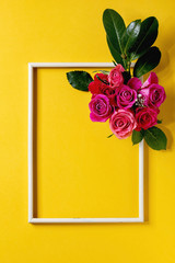 Creative layout with beautiful pink roses flowers and green leaves in wooden frame on bright yellow background. Flat lay. Greeting card concept