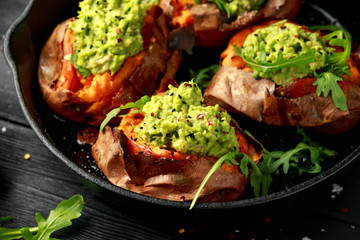 Baked Sweet potato boats stuffed with avocado guacamole and wild rocket sprinkled with nigella seeds in cast iron pan