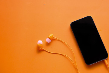 top view of smart phone and headphone on orange background 