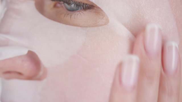 Extreme close up shot of young woman wearing sheet mask gently rubbing her face with her fingers