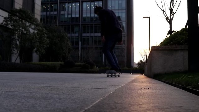 Hombre Joven patinando en skateboard en una plaza frente a un edificio durante el atardecer con los rayos del sol de frente a &eacute;l
