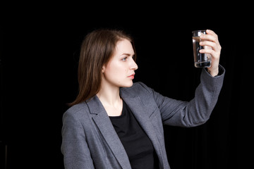 Portrait of a woman looking to the glass of water. Portrait on a black background