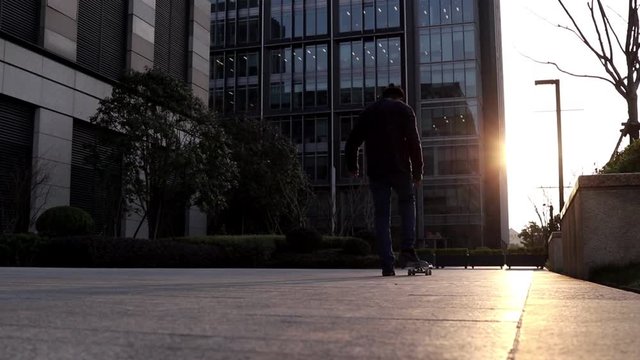 Hombre Joven patinando en skateboard en una plaza frente a un edificio durante el atardecer con los rayos del sol de frente a &eacute;l