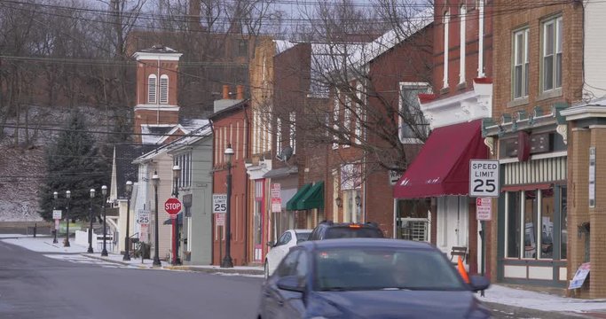 A daytime establishing shot of storefronts along a main street in a small town. Church steeple in distance. Snowing version available.  	