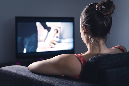Young woman watching horror movie on online stream service. Girl streaming scary film or series at night. Fear and terror during thriller on tv. Video on demand (VOD) technology in television.
