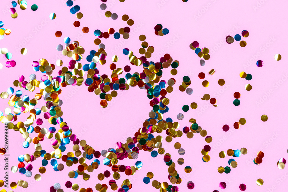 Wall mural Heart shape made of golden colorful confetti splash on pink background. Festive backdrop of sparkles for birthday, valentine's day, carnival