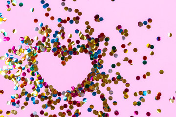Heart shape made of golden colorful confetti splash on pink background. Festive backdrop of sparkles for birthday, valentine's day, carnival