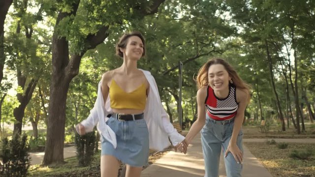 Two positive laughing young girls are running together in the city park