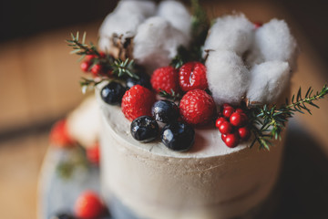 fashionable grey coloured winter theme cake with cotton flowers red berries raspsberries blueberries 