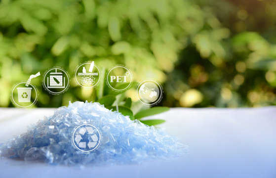 A Pile of PET bottle flakes with green tree blur background.Recycle icon,picking up Plastic Bottle,PET icon&Compress bale icon.Save environment concept