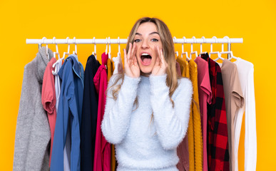 Young woman in a clothing store over isolated yellow background shouting with mouth wide open