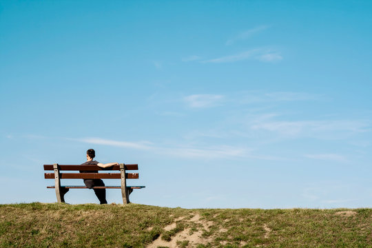 lonely man siting on a bench on an empty landscape