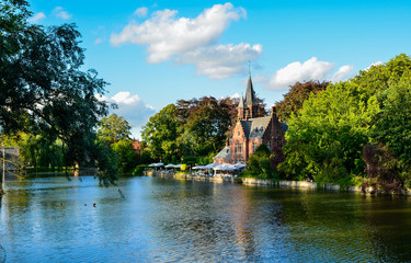 Fototapeta na wymiar Bruges, Belgium. August 2019. The lake and minnewater park are the most romantic place. The body of water on which the red brick castle and the large trees with green foliage are reflected.