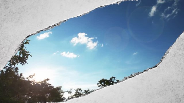 Creative time laps video of fast moving clouds in the blue sky at sunset witn sunflare that are visible through a hole with torn edges in old retro grunge vintage paper.