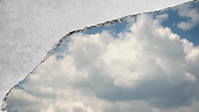 Creative time laps video of fast moving clouds in the blue sky that are visible through a hole with torn edges in old retro grunge vintage paper.