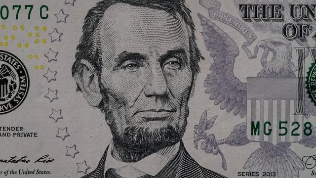 Creative 4k video of five american dollar banknote moving details with a close-up portrait of Abraham Lincoln and the effect of his glowing eyes. USA fiat money. Slow motion.