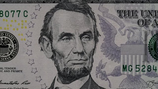 Creative 4k video of five american dollar banknote details with a close-up portrait of Abraham Lincoln, effect of his glowing eyes and a pyramid of 1 dollar banknote. Details of 5 dollar bill.