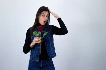 Portrait of attractive caucasian middle age woman with rose being surprised, opening her eyes and mouth with shock, touching her head with hands, isolated on gray background studio shot, black sweater