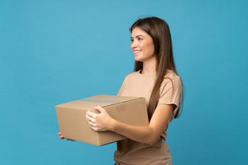 Fototapeta premium Young woman over isolated blue background holding a box to move it to another site