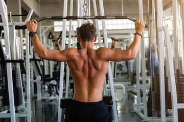 Fototapeta na wymiar Back view of muscular young man doing workout exercise with thrust of the upper block in the gym, training hard in the gym, Athlete makes exercise, Bodybuilder, Sport fitness and muscles concept