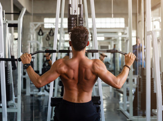Fototapeta na wymiar Back view man doing workout exercise with thrust of the upper block in the gym