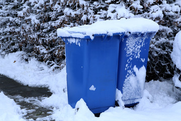 Blue dumpsters stand on a snow-covered street