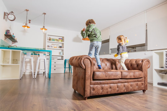 Little Boy And Tiny Blond Girl With Pigtails Dancing On The Couch At Home