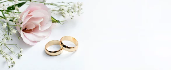 Foto op Plexiglas Roze bloemen en twee gouden trouwringen op witte achtergrond. © Hazal