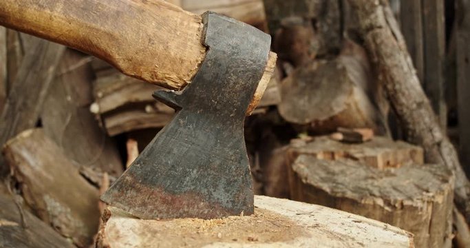 A metal ax is stuck in a log. Brown firewood lies in the background, they are a source of heat and energy in village houses.