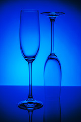 Two empty champagne glasses with reflection, on dark blue and black background gradient background. Concept, party and club life.