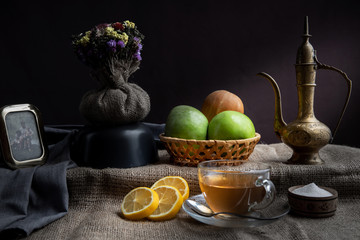 Still life, morning tea with lemons and apples in a homely atmosphere, in dark colors with bright lighting.
