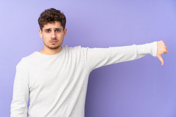 Caucasian man isolated on purple background showing thumb down with negative expression