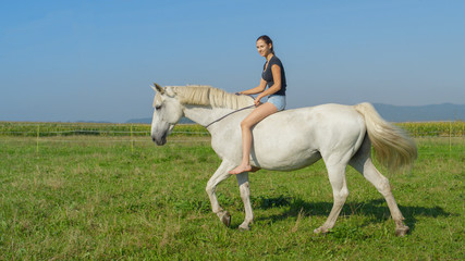 Naklejka na ściany i meble Girl on beautiful white horse bareback riding on grass field