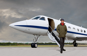 Handsome man standing outside a private jet.