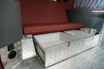 The interior of the car in the back of a van converted into a motor home for off-road and travel with a brown leather interior, a folding table and aluminum floor trim.