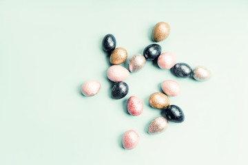 Colored painted pearl chicken and quail eggs of pink, silver, golden and blue color on a light blue pastel background. Minimalistic creative classic easter festive flat lay. Copyspace for text